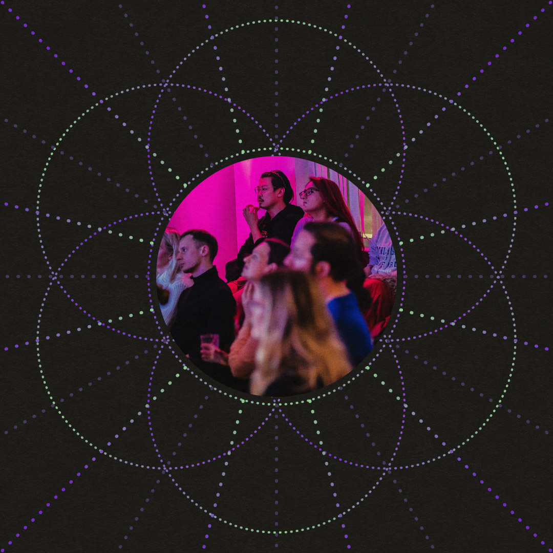 A social post of a a group of people engaged in one of the community events, framed by a 'Seed of Life' geometric pattern with dotted lines in purple and green colours on a dark background. The central circular cutout focuses on the attendees, highlighting their engagement and attention, set against the psychedelic-themed design.