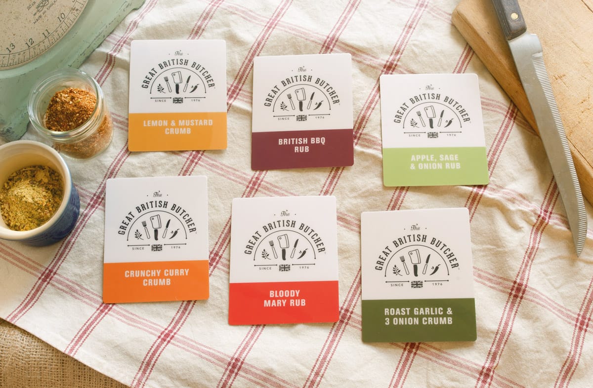 6 point of sale cards for each product flavour laid out on a check table cloth with traidtional utensils surrounding them