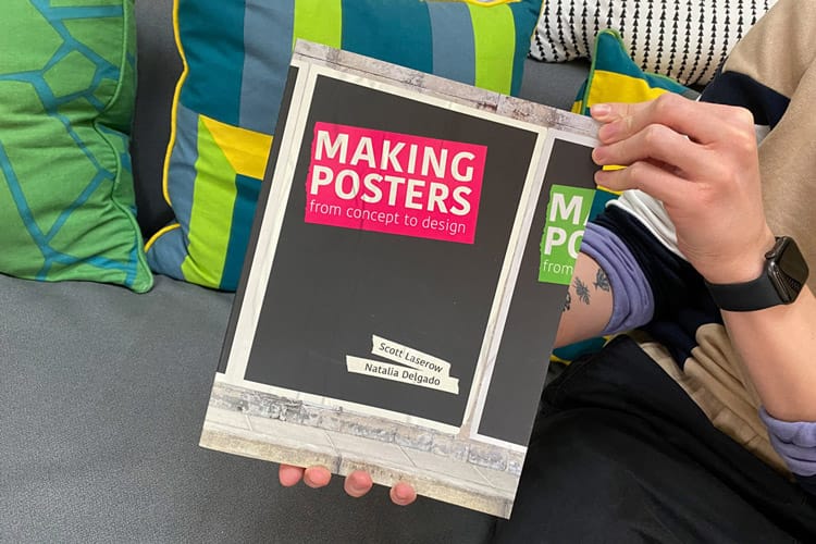 A cropped shot of a persons arms whilst sat on a sofa holding the book entitled 'Making Posters; From Concept to Design".